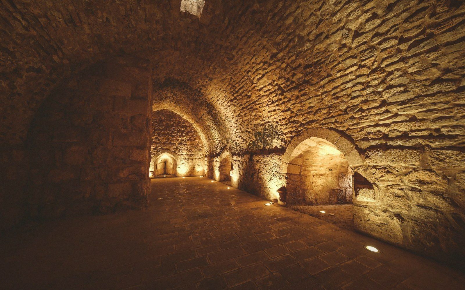 Stone-vaulted underground corridor lined with arched alcoves and warm ambient lighting