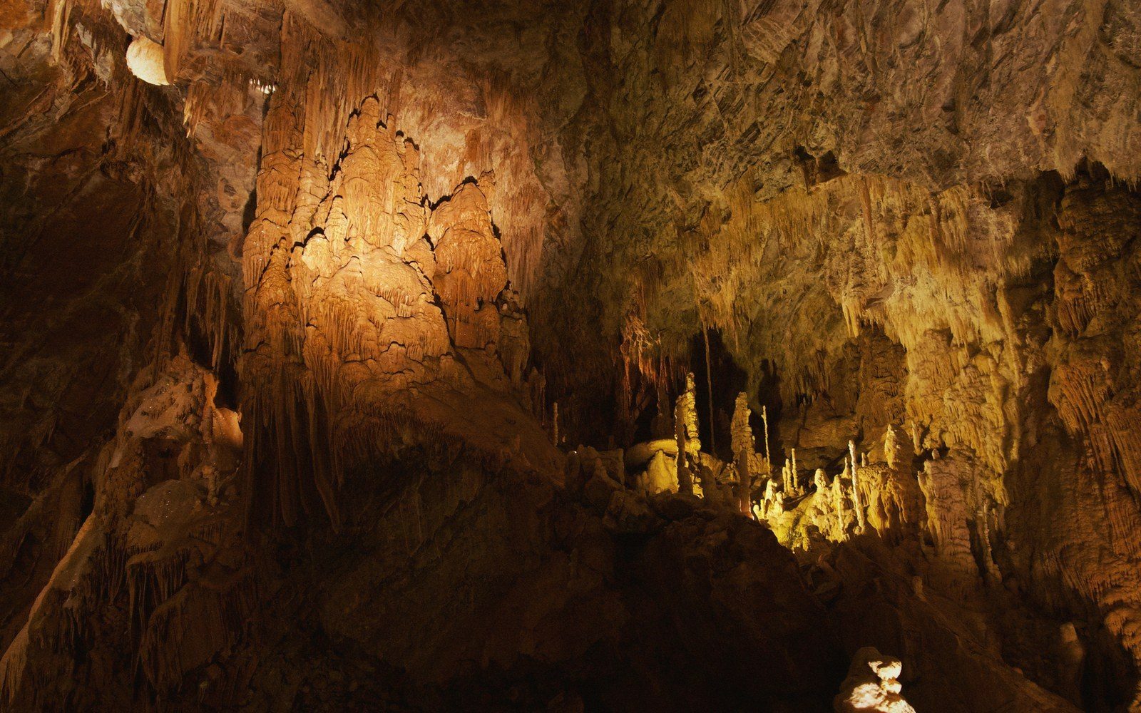 Illuminated limestone formations and stalagmites rise from the floor of a cave chamber